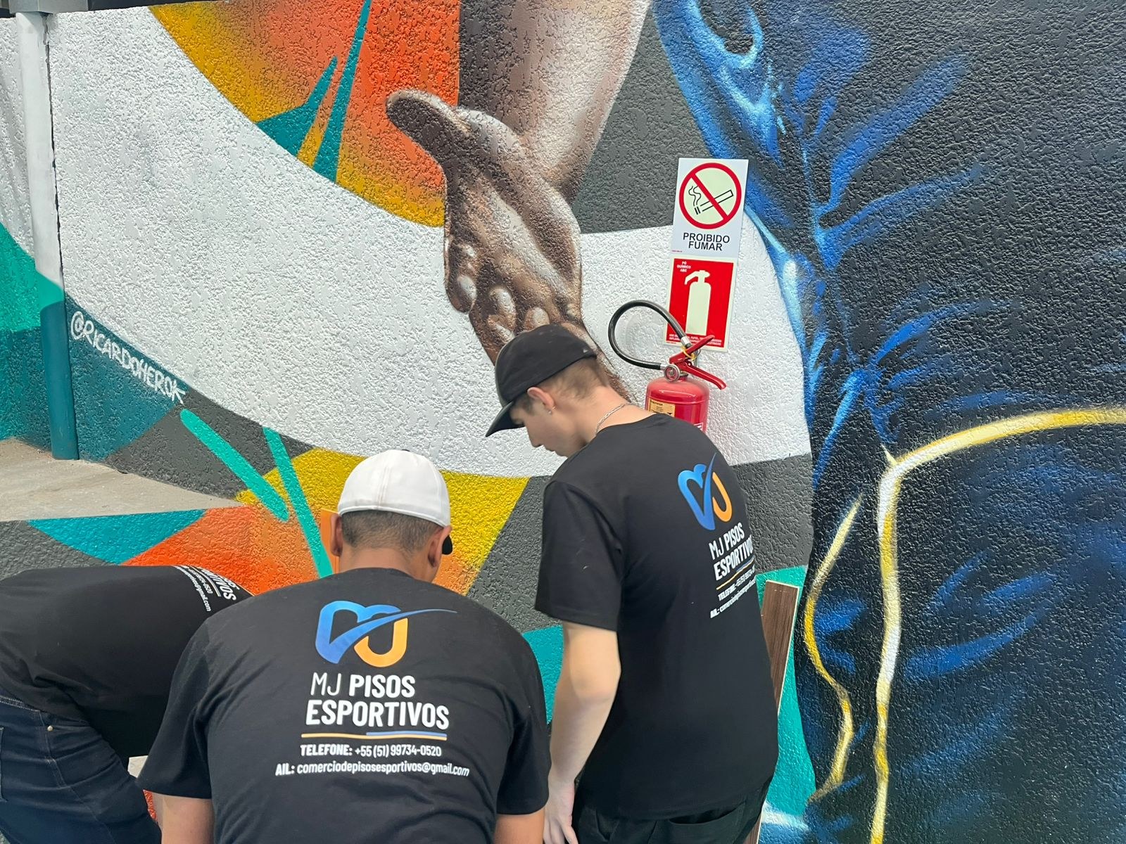 Equipe da MJ Pisos Esportivos trabalhando ao lado de um mural esportivo